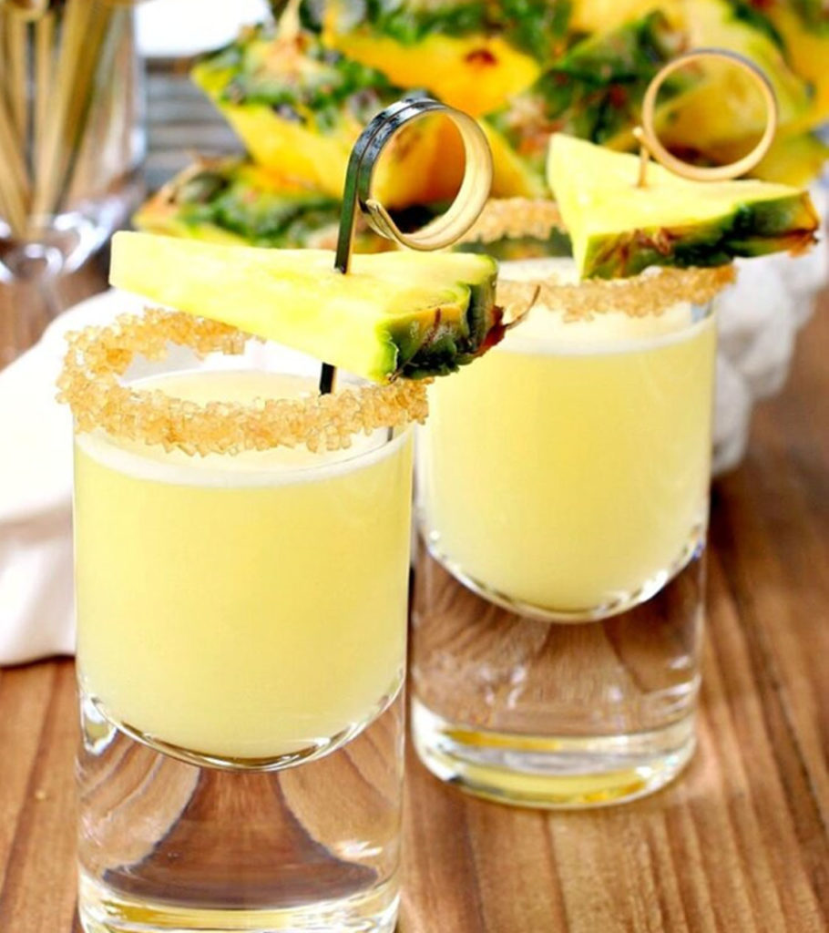 Pineapple shooters with pineapple garnish and sugar rims.