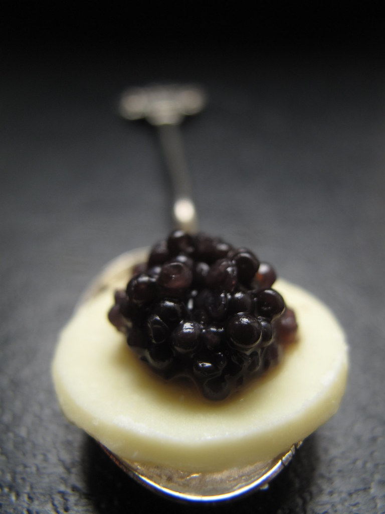 A white chocolate disc with caviar served on a spoon.